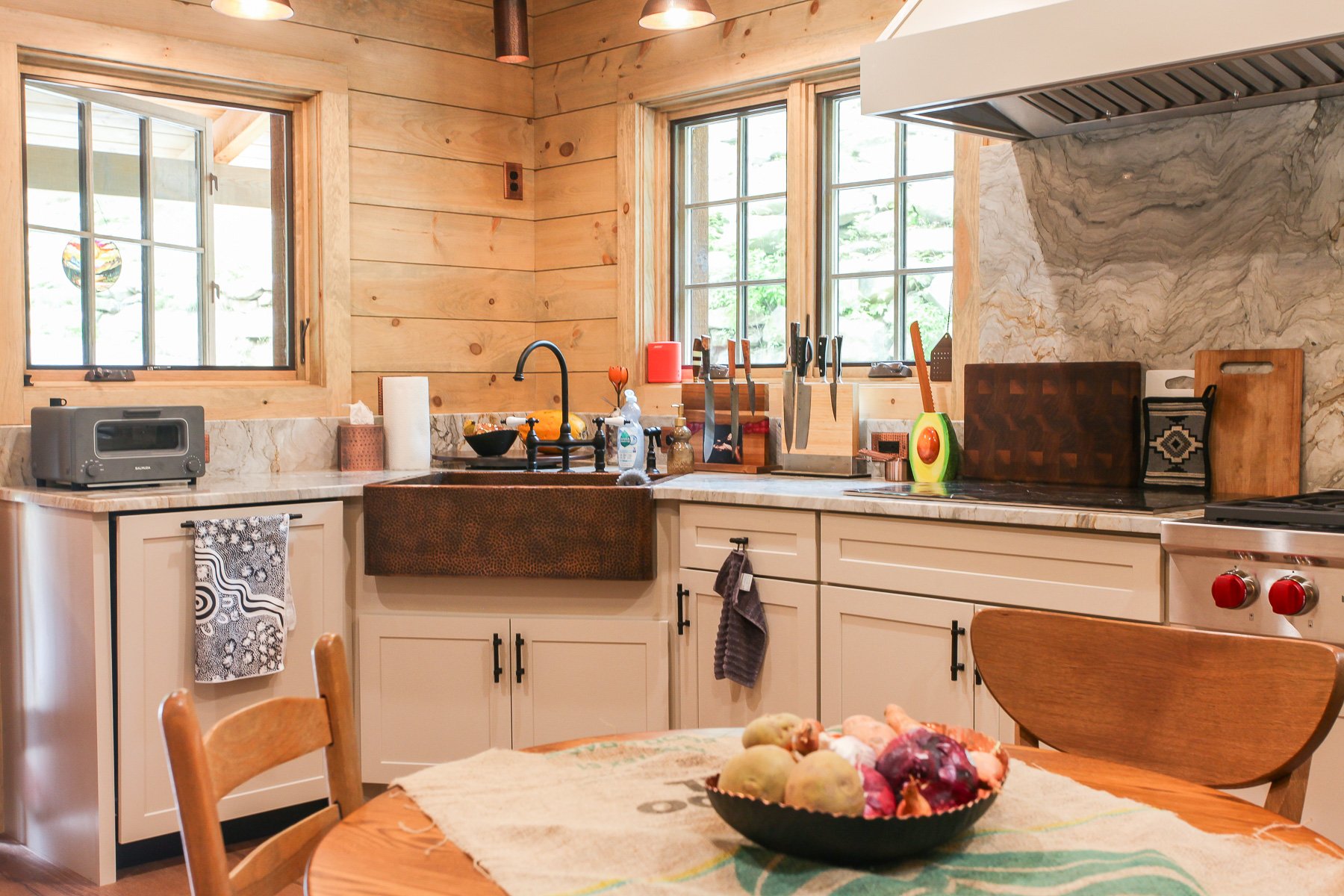 dining table with fruit basket and corner of kitchen with farmhouse sink and windows
