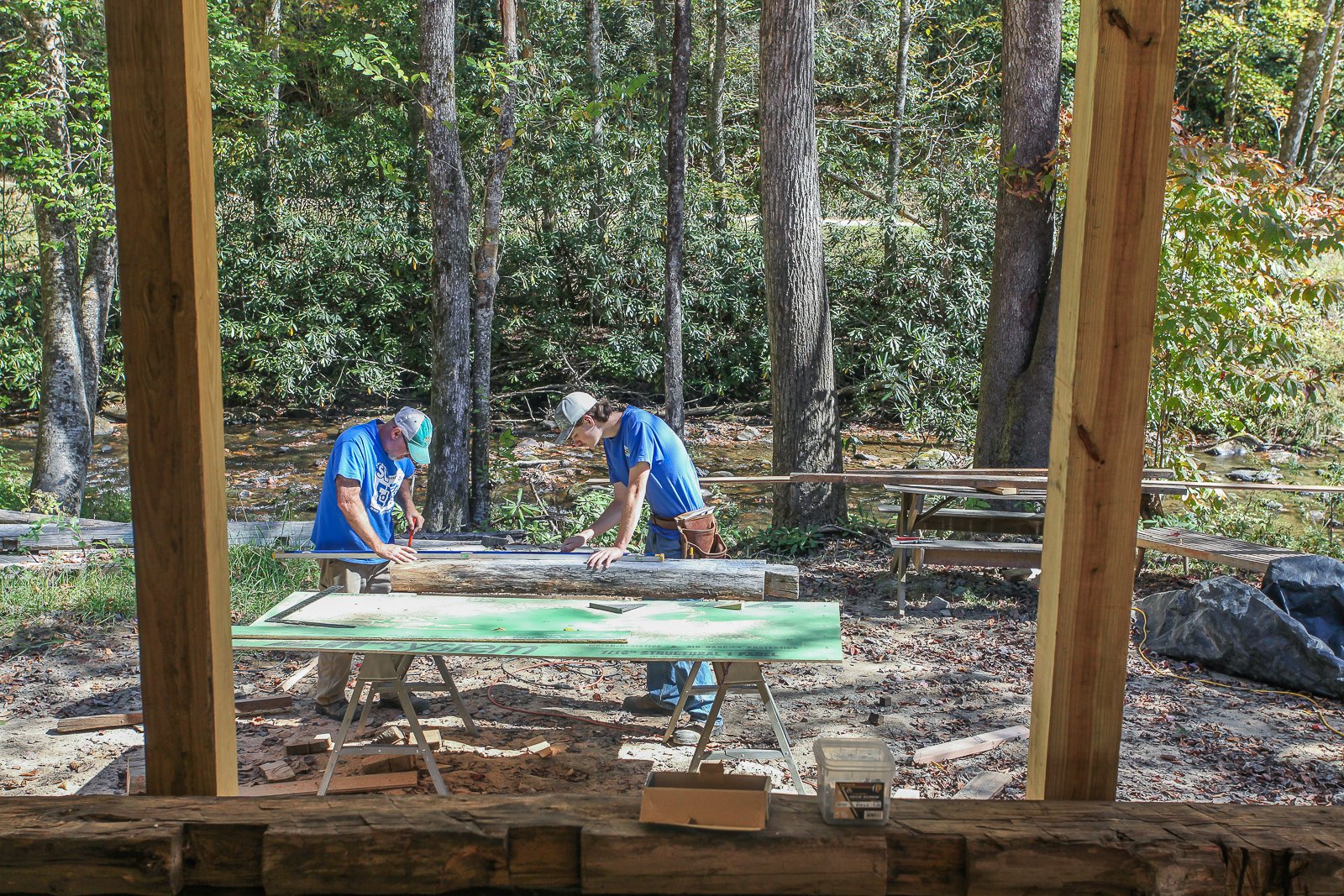 two carpenters cutting and measuring logs for placement on cabin